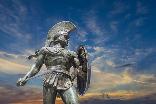 Metal statue of a Roman soldier with sword and shield in front of sunset