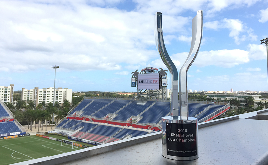 FIFA SheBelieves Champion Cup sitting on a ledge overlooking a soccer stadium. Designed by Gabrielle Rein of Viceroy Creative.