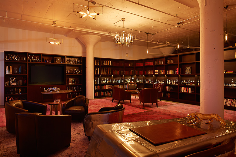 Wide view of our Whiskey Library with overdyed rugs, leather chairs, hanging brass light fixtures, custom wood shelves