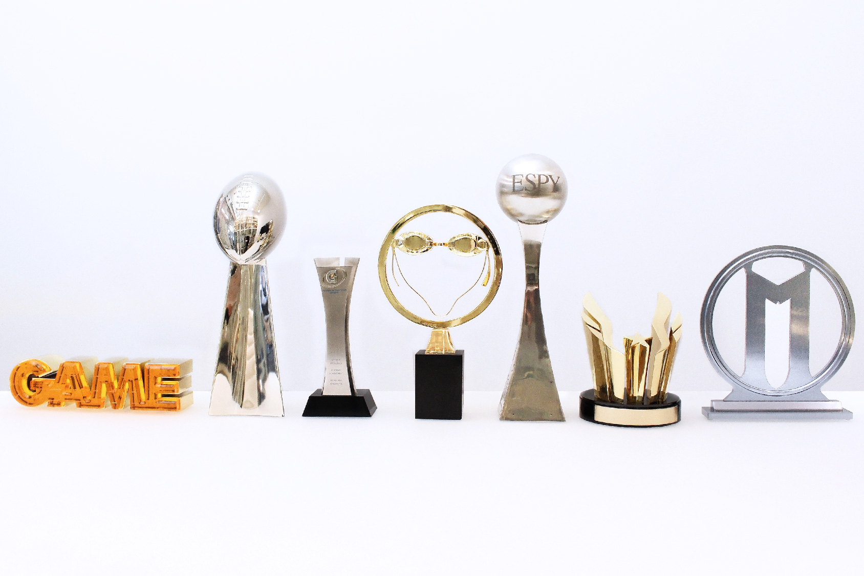 Six custom sports trophies by Society Awards grouped in a line on a white table
