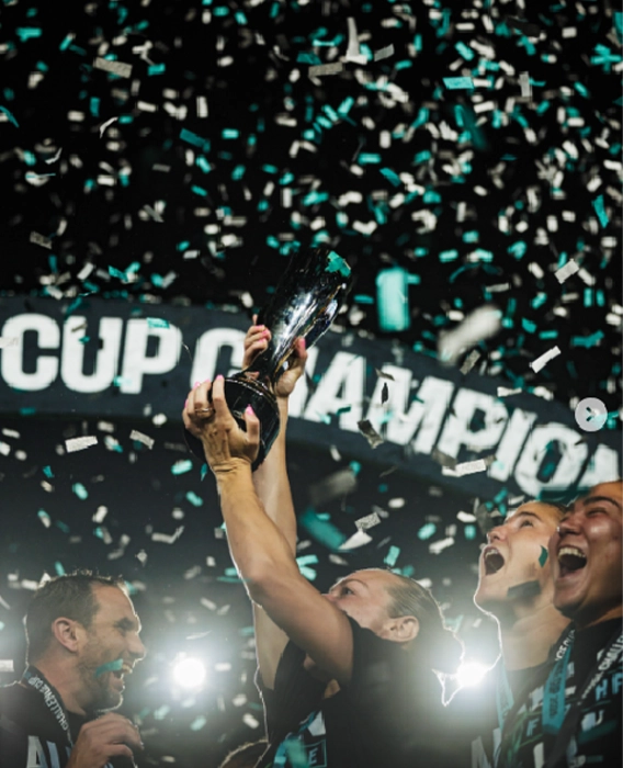 Kansas City Current holding up the new NWSL Challenge Cup as blue and white confetti falls