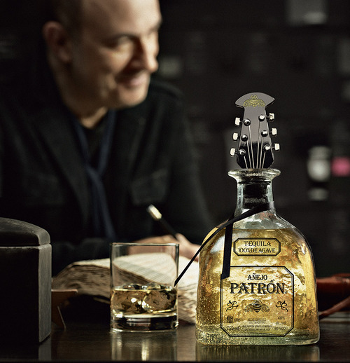 A bottle of Patrón Añejo with the limited edition guitar-head-shaped bottle stopper sitting on a table in front of designer John Varvatos