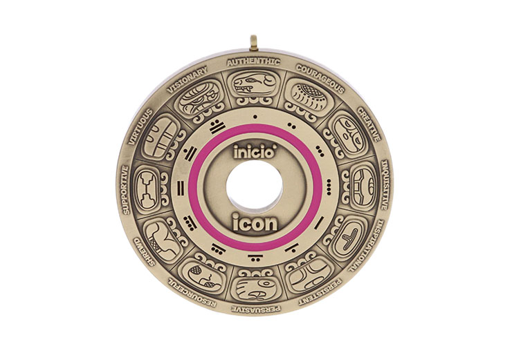 Gold medallion with layers of words and depictions from the outside to the center
