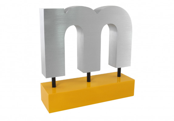 A custom cut metal logo award in the shape of the letter 'm' mounted on an orange base.