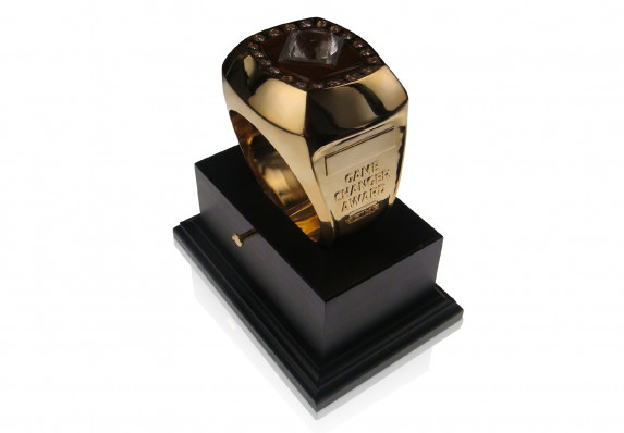 This custom metal trophy is in the shape of a large gold ring with inlaid crystal gems and colorful enamel. It is presented on an exceptional stepped wood base.