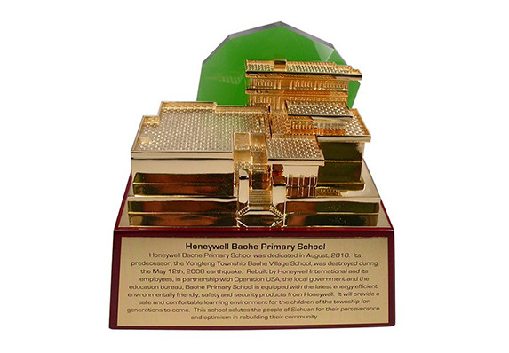 gold plated replica of a charity built school with green crystal mountain accent on cherry piano wood base