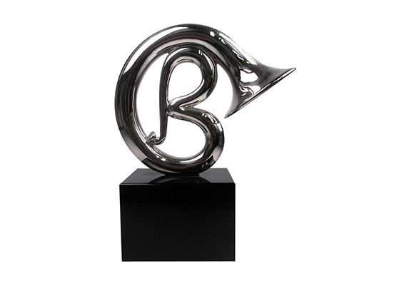 Trumpet custom designed to incorporate logo 'B' in shiny silver metal. The sculptural form is mounted on a black crystal base.