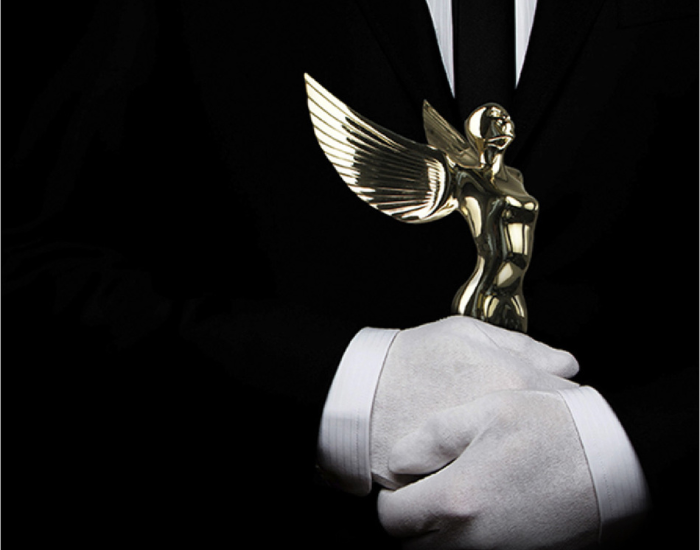 White glove concierge in a black and white suit holding a gold angel trophy award