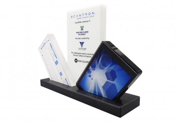 A custom acrylic financial tombstone with models and a central plaque with acquisition details.