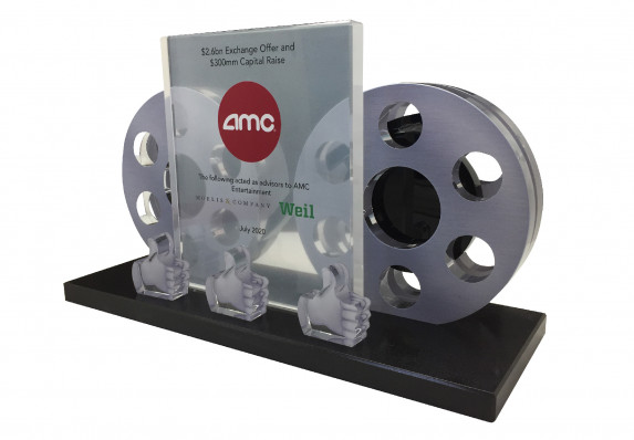 A custom deal toy with two film reels presented on a crystal base alongside a printed financial tombstone plaque.
