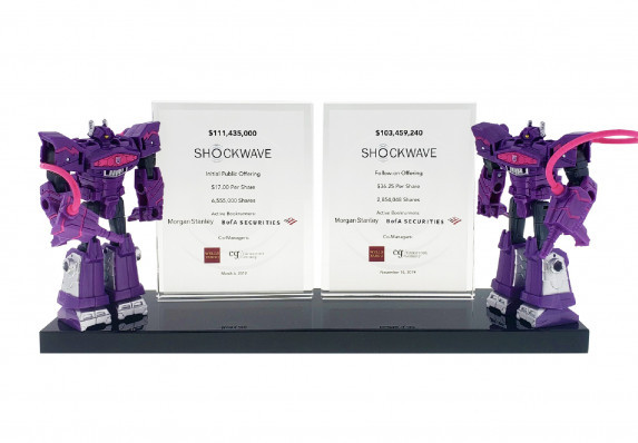Double crystal deal tombstone plaques mounted on a base alongside two robot figurines presented for an initial public offering.