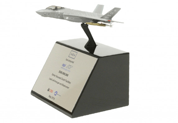 A model fighter jet is presented on an elegant tapered base in this exceptional financial tombstone for an acquisition deal.
