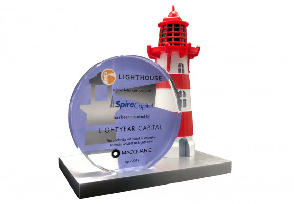 A financial tombstone printed on a color printed plaque and mounted on a base with a detailed model lighthouse.