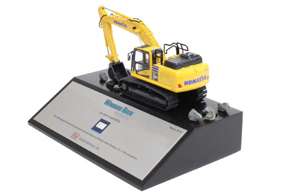 A scale model yellow digger vehicle mounted on a tapered black base with a silver financial tombstone plaque.